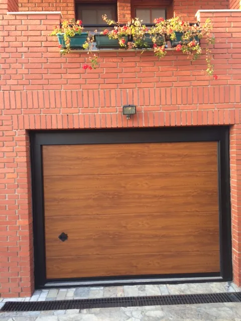 Wood-effect garage door with a black frame in a brick wall
