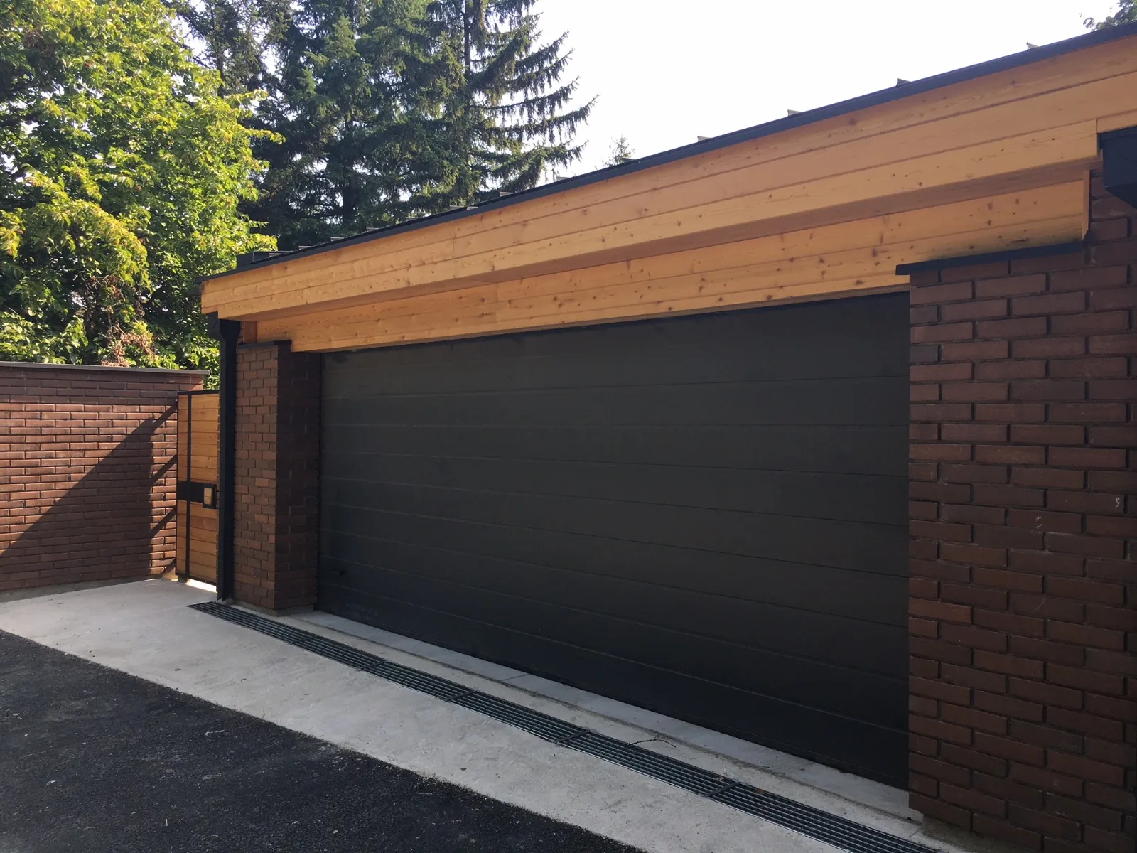 Dark sectional garage door and pedestrian gate beside brick pillars
